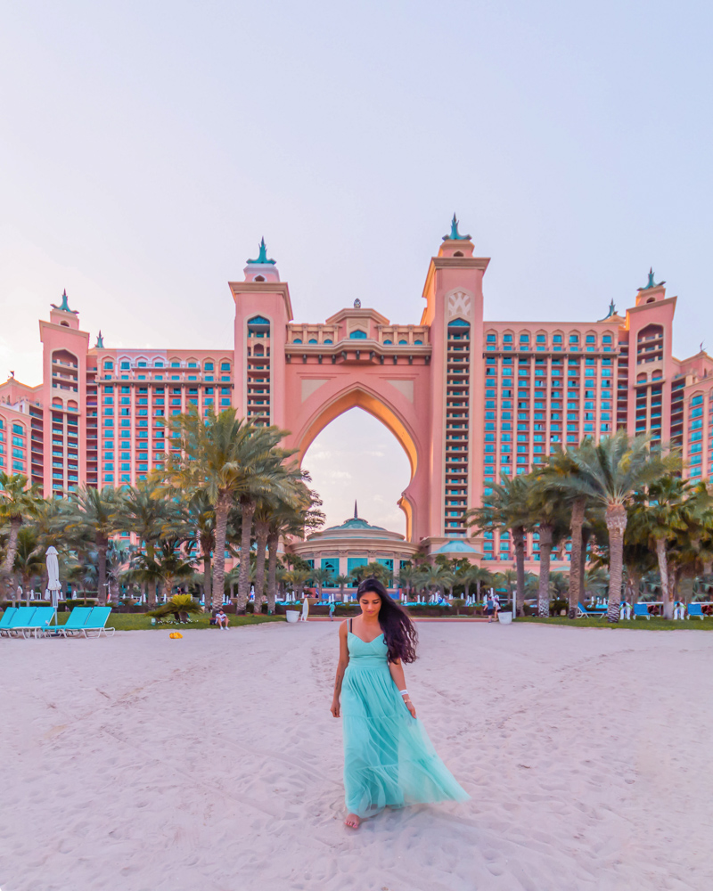 A girl in sage color dress standing at the beach at the back of Atlantis the Palm
