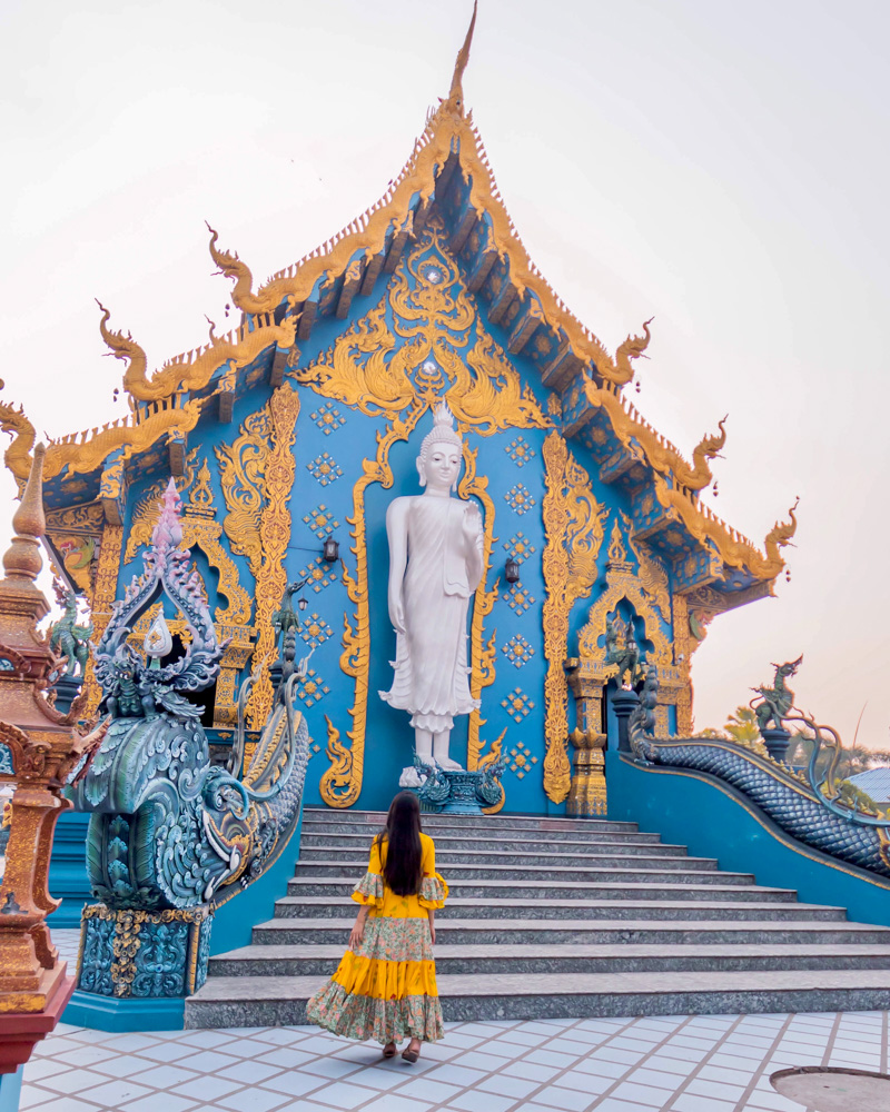 A girl standing at the back of blue temple in front of buddha statue