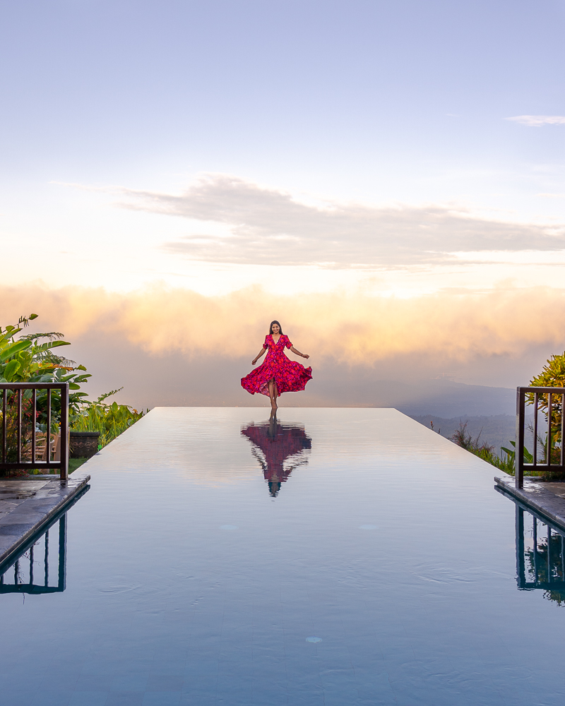 A girl in red dress standing on the edge of infinity pool at munduk moding resort in munduk bali