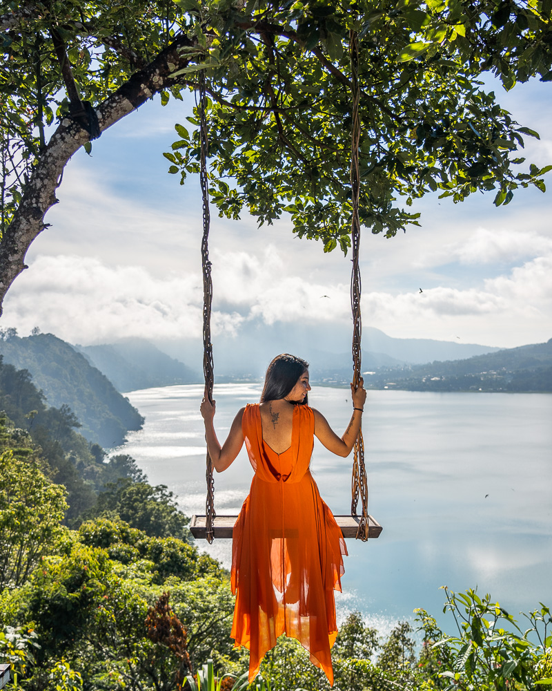 A girl in orange dress sitting on a swing at wanagiri hidden hills in Munduk Bali