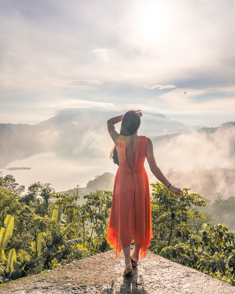 A girl in orange dress standing at a viewpoint overlooking twin lakes in munduk bali
