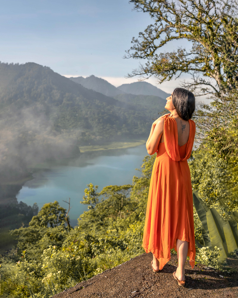 A girl in orange dress standing at a viewpoint overlooking twin lakes in munduk bali