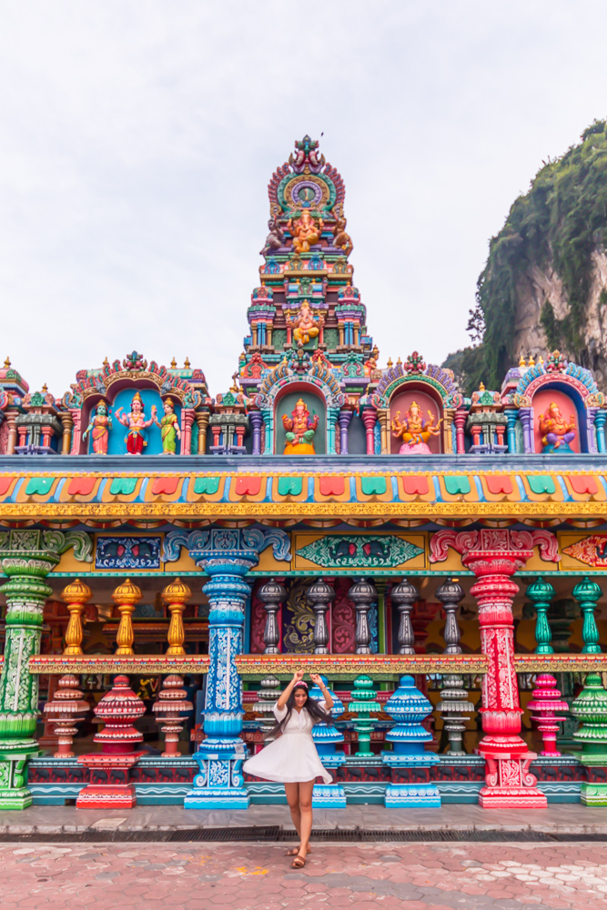 A girl in white dress twirling in front of colorful batu caves in Kuala Lumpur Malaysia