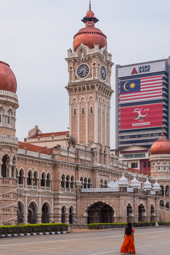 A girl in orange dress standing in front of sultan Abdul Samad building at Merdaka Square in Kuala Lumpur, malaysia