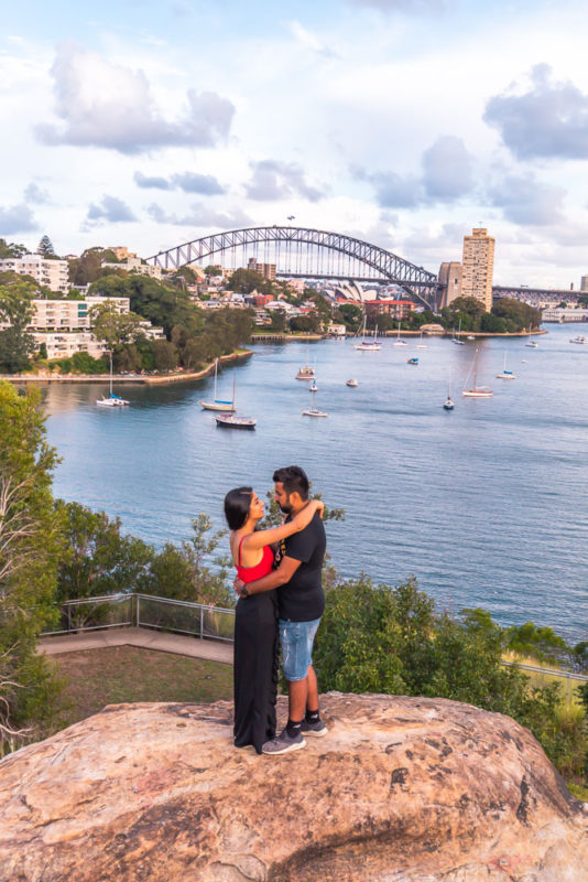 A couple posing on the rock with a view of Sydney Harbour Bridge and sea..