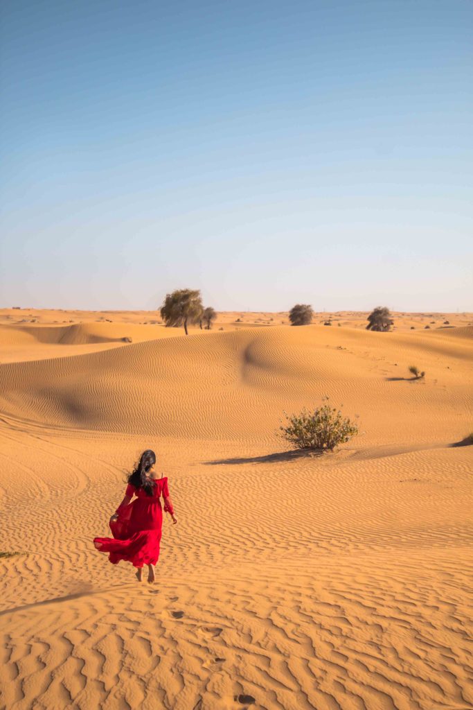 A girl in red dress walking and enjoying the desert