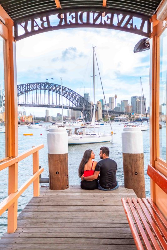 A couple sitting at Lavender Bay Wharf with a view of sydney harbour bridge