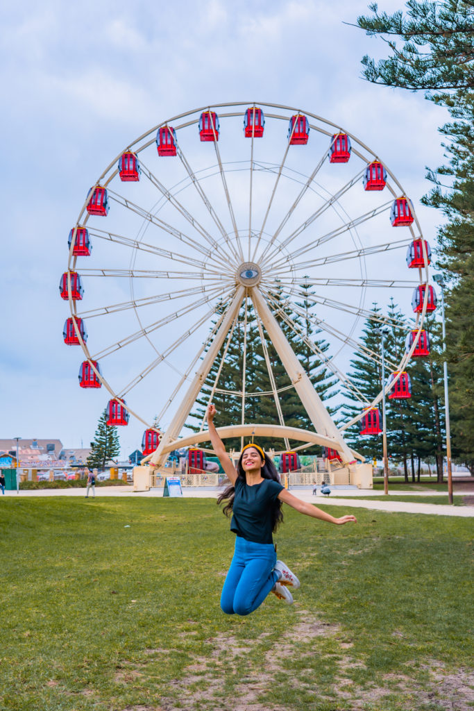 A girl jumping with joy in front of ferris wheel at Esplanade in Fremantle