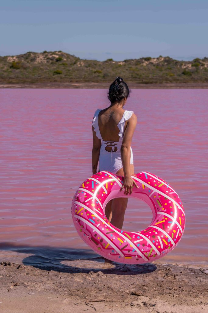 A girl with a donut floaty and the view of Hutt Lagoon Pink lake
