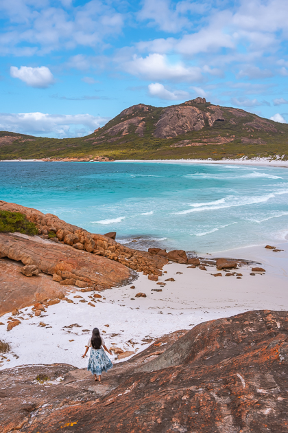 A girl standing at the granite boulders watching the turquoise water of Thistle Cove, one of the best beach in Esperance