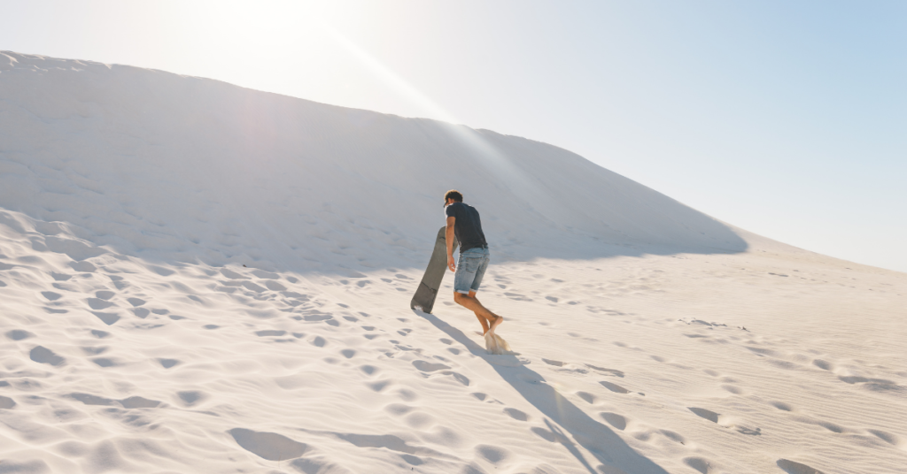 A man taking the sandboard to the top of lancelin sand dunes