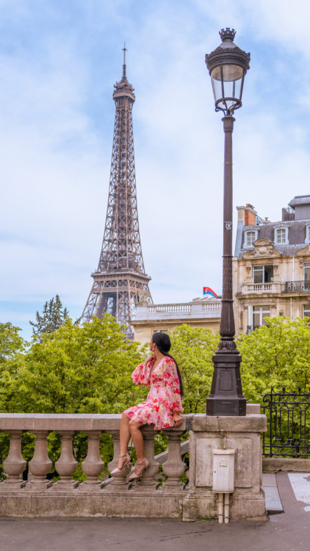 A girl in a pink dress sitting on a ledge looking at the Eiffel tower