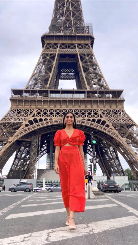A girl in orange set standing in front of the Eiffel tower