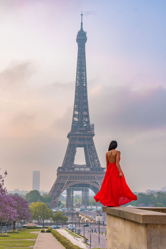A girl in a red dress standing on a platform with a view of the Eiffel tower